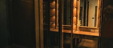 A glass-walled elevator with a mirrored interior, reflecting a hallway with a door and a light fixture.