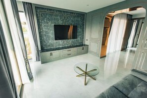 A modern living room with a flat-screen TV mounted on a wall, a glass coffee table, and a grey sofa. - Astro Luxury: 4-6 beds Ultra Luxury Pool Villa with Daily Cleaning (Pattaya)