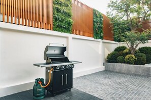 Una parrilla portátil con tanque de gas y manguera, ubicada en un patio con baldosas.