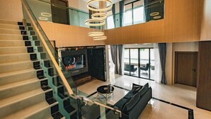 A modern interior with a glass staircase, a living area with a flat-screen TV, and a dining space with a glass table. - Astro Luxury: 4-6 beds Ultra Luxury Pool Villa with Daily Cleaning (Pattaya)