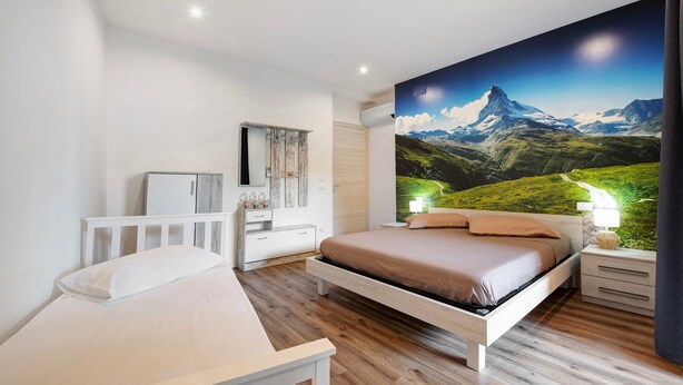 A bedroom with a bed, bedside table, dresser, and a large wall mural of a mountain landscape.