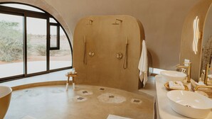 A modern bathroom with a large window, a curved shower, and a vanity with multiple sinks. - Reverie - Kalahari Pod (Mariental)