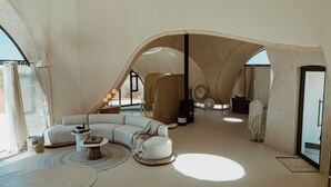 A spacious living area with a curved ceiling, a sectional sofa, a coffee table, and a round table. - Reverie - Kalahari Pod (Mariental)