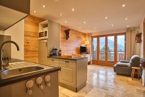 A kitchen with a sink, stove, and microwave, a dining area with a table and chairs, and a balcony with a view of the mountains. - Apartment 'Résidence 17' with Mountain View and Balcony (Les Deux Alpes)