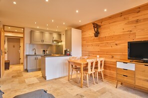 Een moderne keuken met houten kastjes, een eethoek met een houten tafel en stoelen, en een televisie op een houten kast.