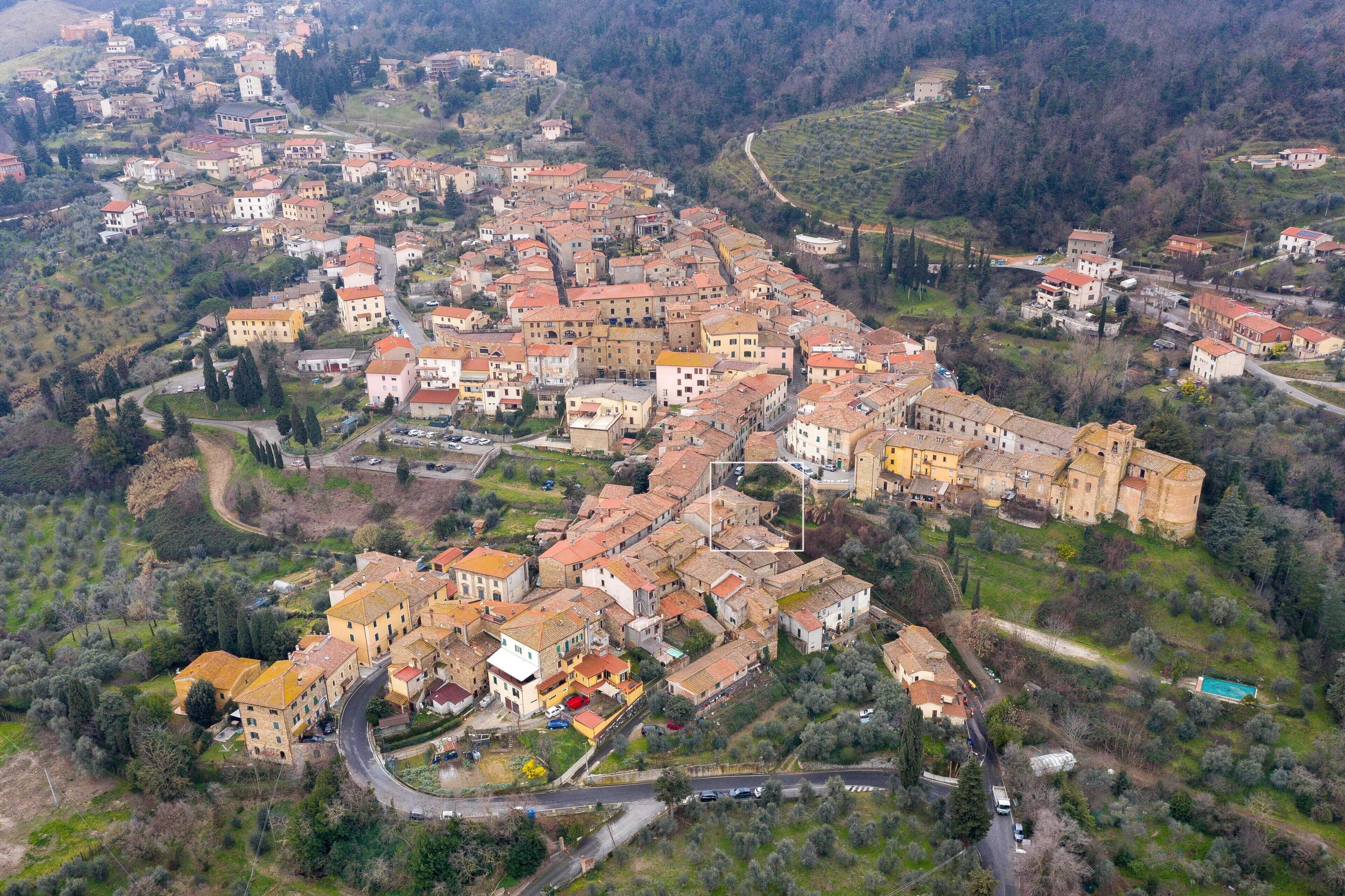 An aerial view of a historic town with closely packed buildings, winding roads, and surrounding greenery.