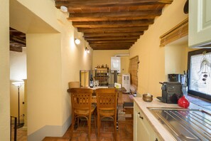 A narrow kitchen with wooden chairs, a dining table, and a tiled floor.