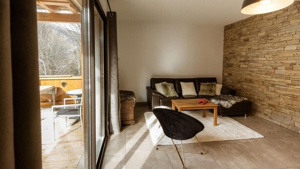 A modern living room with a stone wall, a leather sofa, a wooden coffee table, and a black chair.
