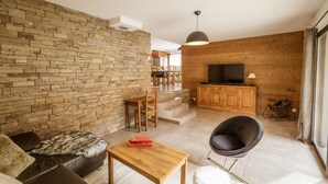 A living room with a stone wall, a wooden TV stand, a leather sofa, a wooden coffee table, and a black chair.