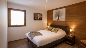 A bedroom with a large bed, wooden walls, a window, and two wall-mounted paintings.