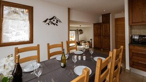 A dining area with a table set for four, wooden chairs, a bottle of wine, and a decorative wall piece.