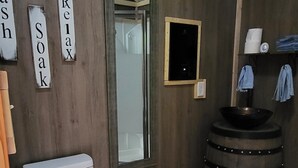A bathroom with a toilet, a wooden vanity, a mirror, and a sink with a barrel-style base.