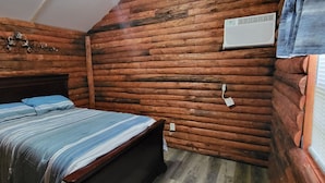 A log cabin room with a bed, wooden walls, a decorative wall piece, and an air conditioning unit.