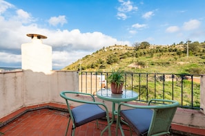 Um terraço com mesa e cadeiras, um vaso de planta e vista para uma paisagem montanhosa.