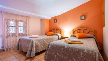 Una habitación con dos camas, una ventana con cortinas, un cabecero de madera y una mesita de noche con lámpara.