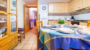 A kitchen with wooden cabinets, a dining table set with plates, a clock on the wall, and a refrigerator. - Country House 'Casa Lino' with Mountain View, Private Terrace and Wi-Fi (Culla)