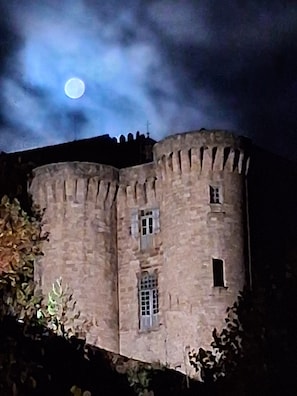 A stone castle with a round tower, a window with a grille, and a moon in the sky.
