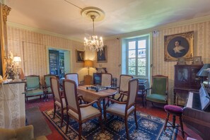 A room with a chessboard, chairs, a piano, and a chandelier.