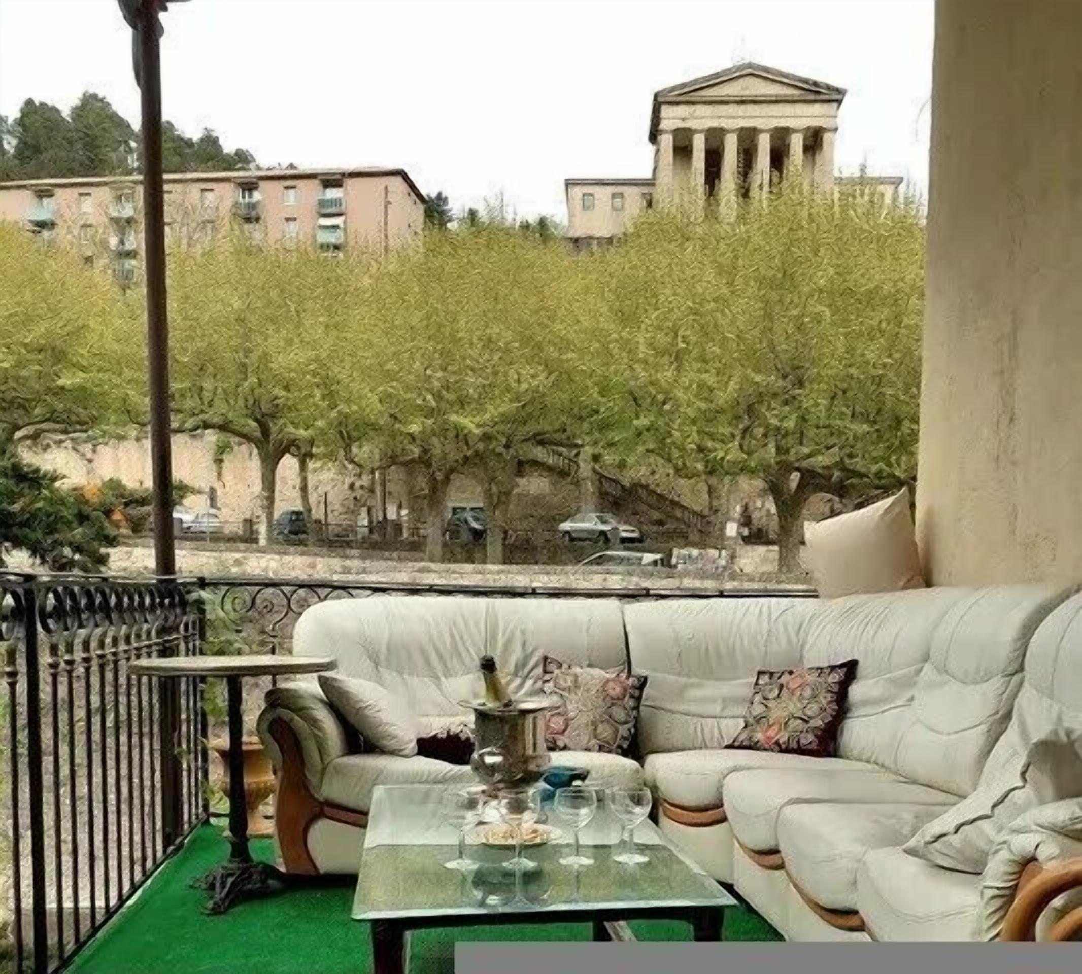 A balcony with a white sofa, a small table, and a view of trees and buildings.