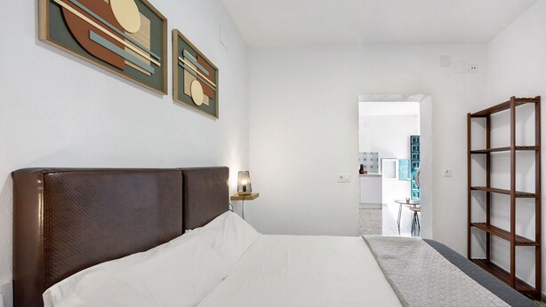 A bedroom with a large bed, a nightstand with a lamp, and abstract wall art. - Cozy Vacation Rental in Chiclana de la Frontera (Chiclana de la Frontera)