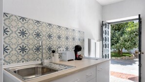 A kitchen with a stainless steel sink, white cabinets, a patterned backsplash, and a view of a garden through an open door. - Cozy Vacation Rental in Chiclana de la Frontera (Chiclana de la Frontera)