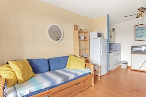 Un espace de vie compact comprenant un canapé, un petit coin cuisine et un miroir rond accroché au mur.