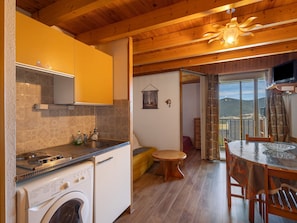 A kitchen with a washing machine, wooden ceiling, and a dining area with a table and chairs.
