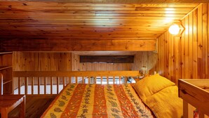 Interior de una cabaña de madera con literas, techo de madera y una lámpara.