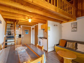 A wooden interior with a dining table, a sofa, a washing machine, and a kitchen area. - Apartment 'Face Au Lac 6 Voyageurs' with Lake View and Balcony (Les Angles)