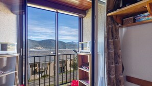 Un balcón con vistas a montañas distantes, un microondas en la barandilla y una estantería con libros.