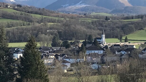 Ein Dorf mit einer Kirche, umgeben von Bergen und viel Grün.