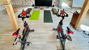 Een zolderkamer met twee stilstaande fietsen, een projectiescherm en fitmatten.