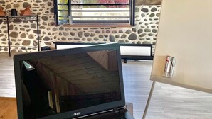 Een laptop op een tafel in een kamer met een stenen muur, een raam met uitzicht op bomen en een houten plafond.
