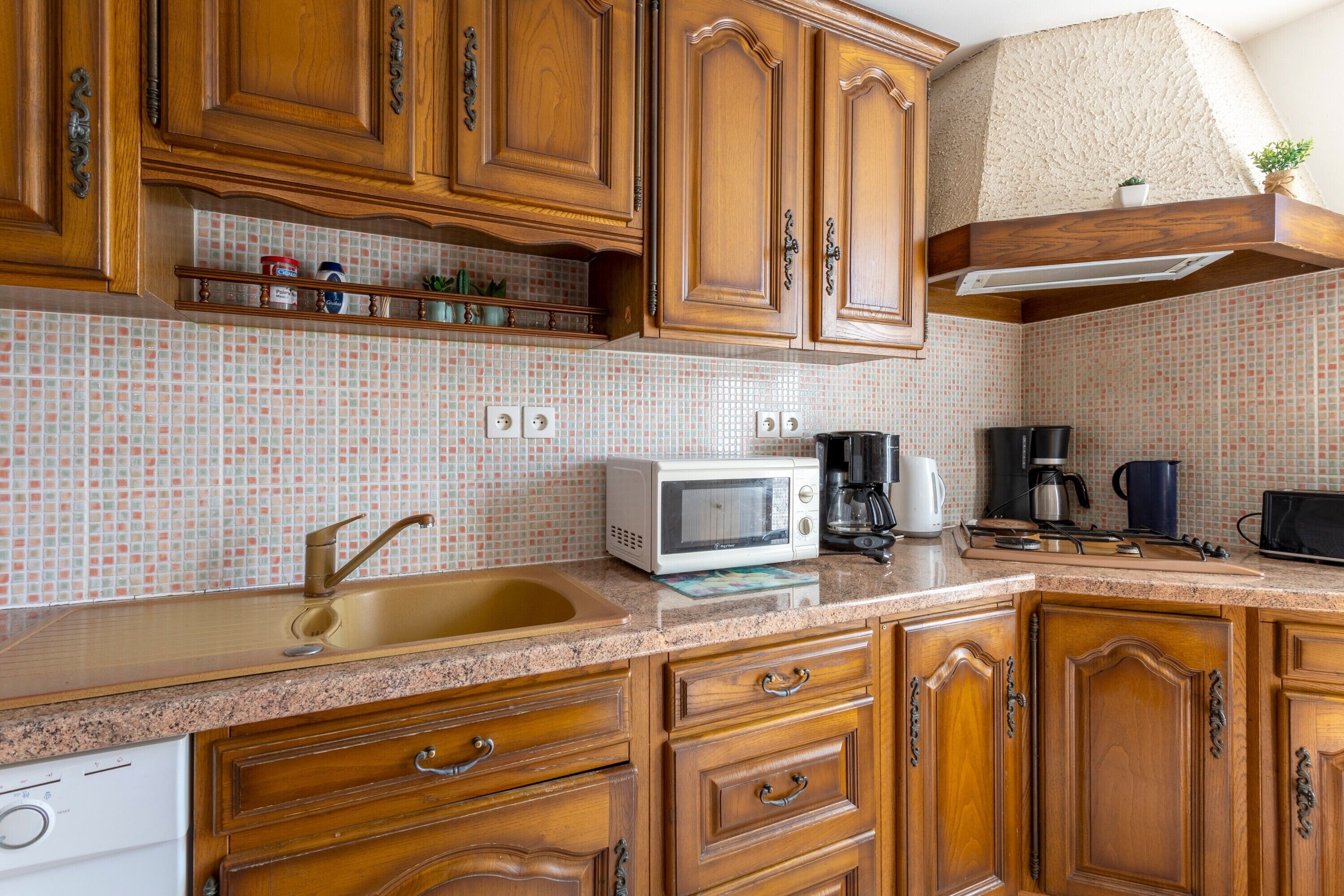 Una cocina con armarios de madera, microondas, cafetera y lavabo.