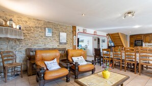 A stone-walled room with two leather armchairs, a wooden coffee table, and a dining area with wooden chairs and a table. - Holiday Home 800 m From the Beach with Private Terrace and Private Garden (Penmarc'h)