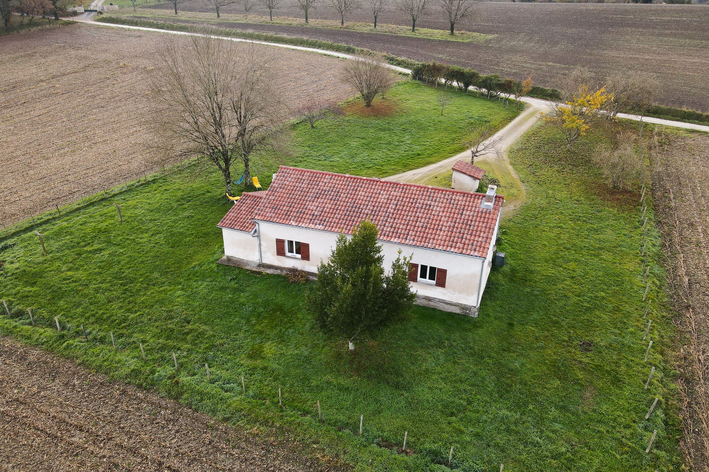 A single-story house with a red-tiled roof, surrounded by a well-maintained lawn and a fenced property.