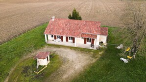 Una casa de un piso con techo de tejas rojas, un porche pequeño y un patio cercado.