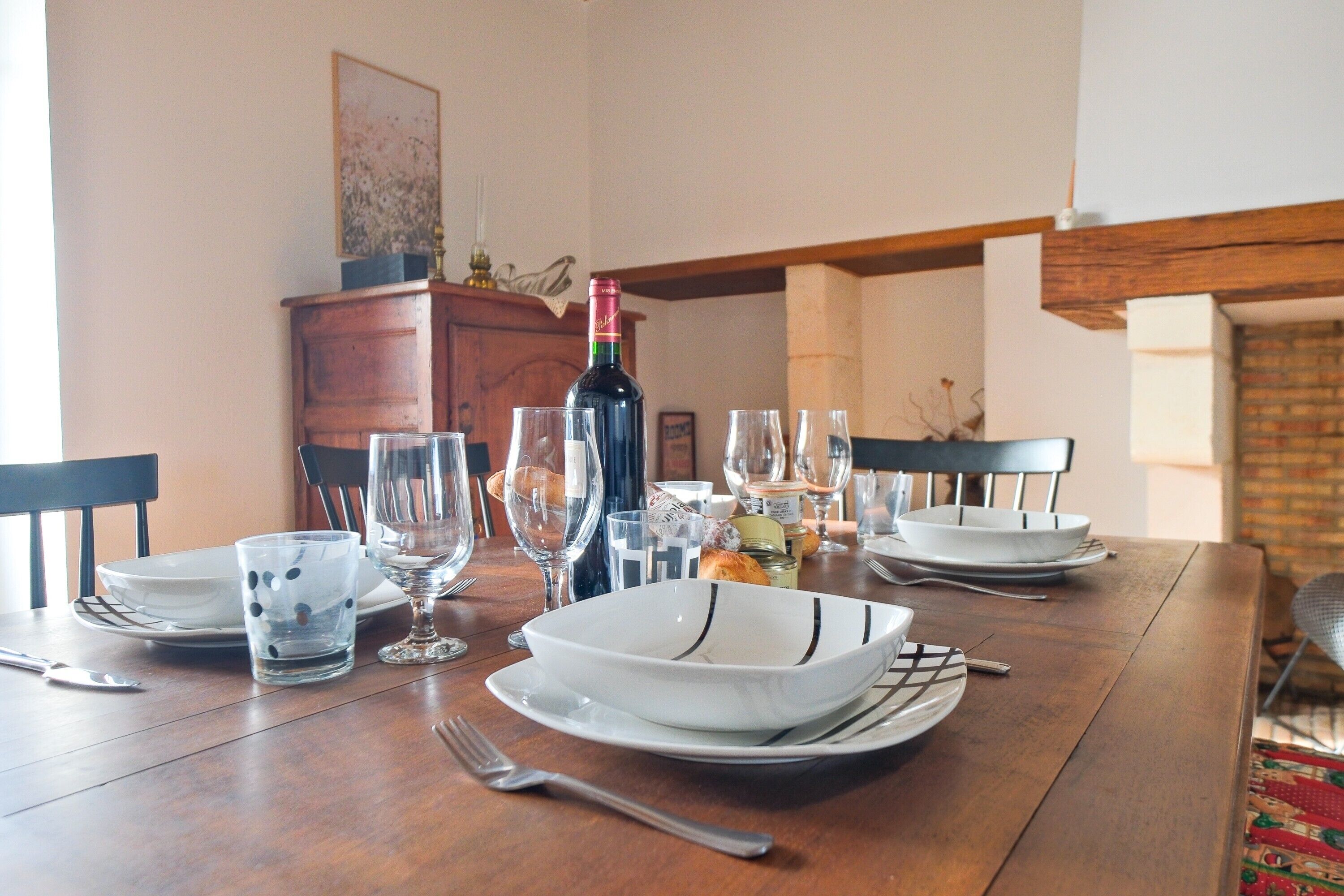 Une table à manger dressée avec des assiettes, des bols, des verres et des couverts, ainsi qu’une bouteille de vin et un objet décoratif posés sur la table.