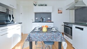 Una cocina moderna con armarios blancos, un microondas, una estufa y una mesa de comedor preparada para cuatro personas.