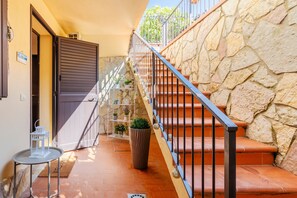 Un escalier avec des murs en pierre, une rampe métallique et une porte donnant sur une pièce.