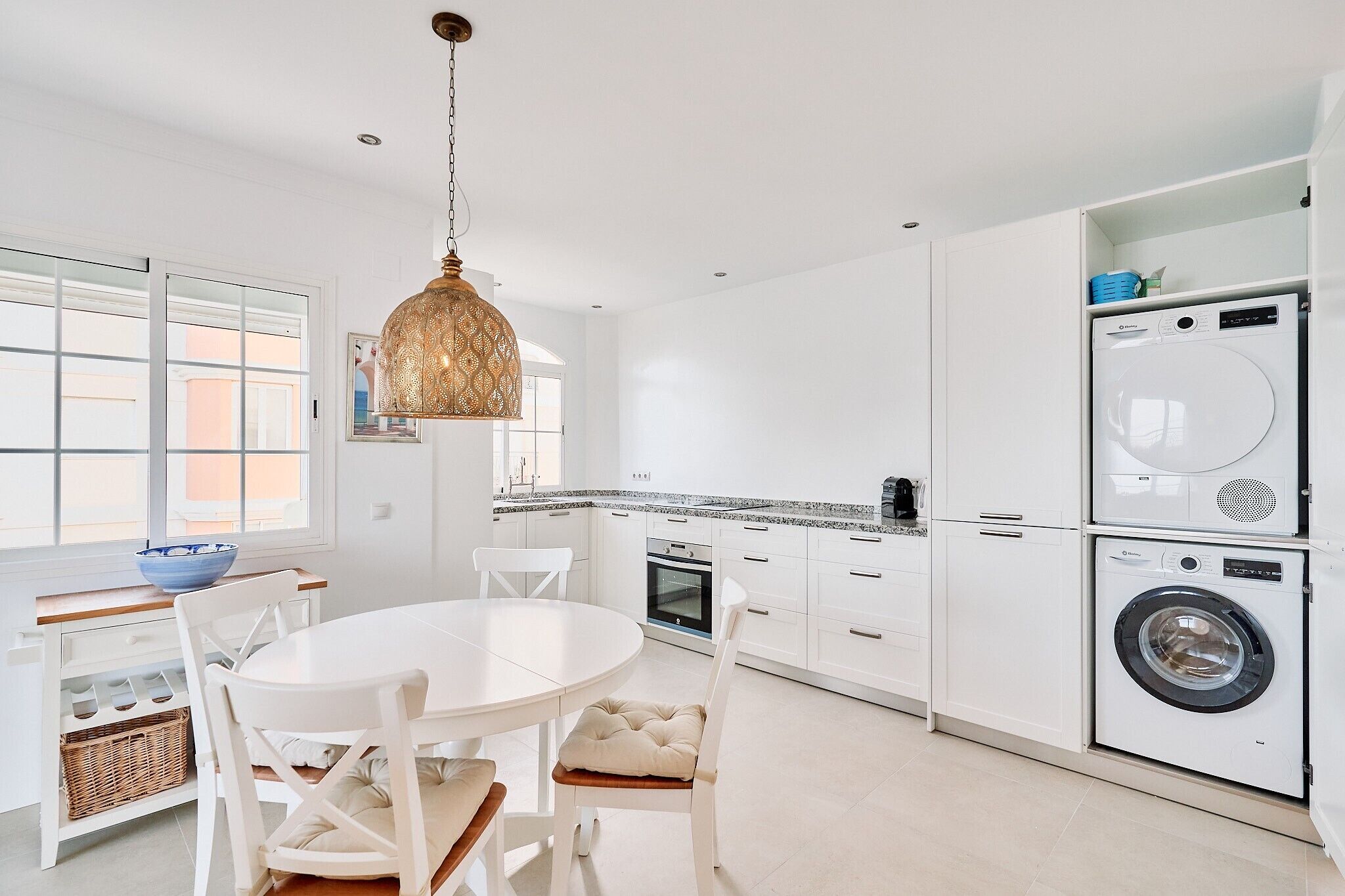 A modern kitchen with white cabinets, a dining table, and a hanging light fixture.