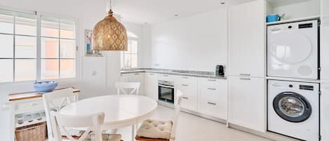 A modern kitchen with white cabinets, a dining table, and a hanging light fixture.