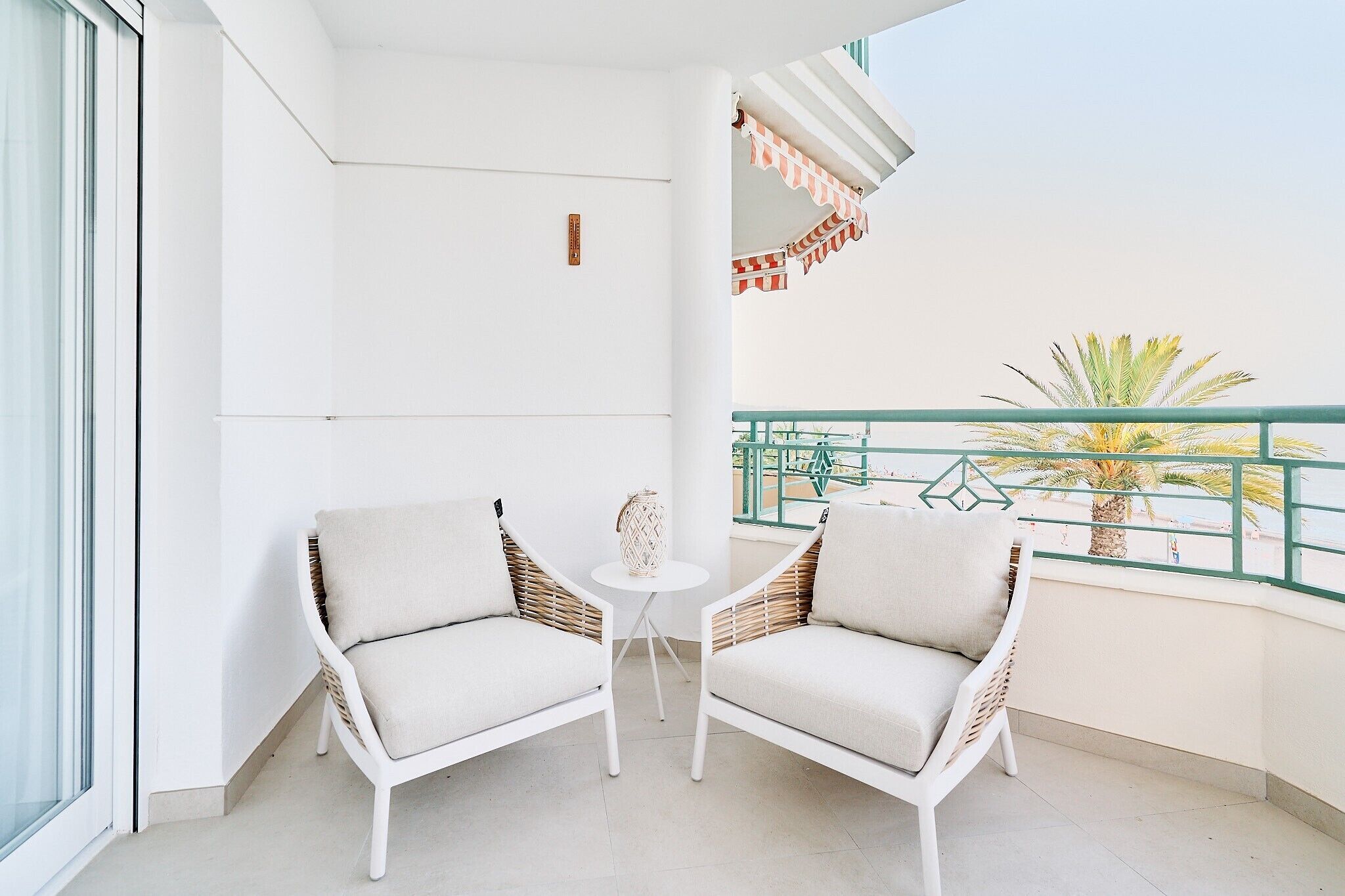 Ein Balkon mit zwei weißen Korbstühlen, einem kleinen runden Tisch und einer Zierblume.