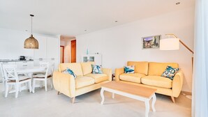 Un salon moderne avec deux canapés jaunes, une table basse en bois, une table à manger avec des chaises, un luminaire suspendu et une lampe sur pied.