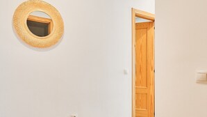 Un couloir avec une porte en bois, un miroir fixé au mur et un interrupteur.