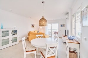A dining area with a round table, white chairs, a hanging light fixture, a sofa, and a cabinet with glass doors. - Apartment 'First Line Oasis  Td05' with Sea View, Wi-Fi and Air Conditioning (Torrox)