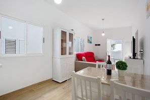 A modern living room with a dining area, white furniture, a red sofa, and a small table with a bottle.