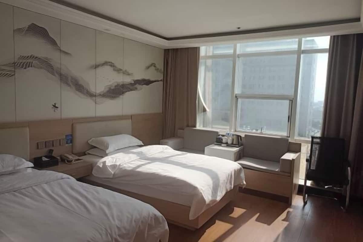 A hotel room with two beds, a large window, a wall with artwork, and a view of the city.