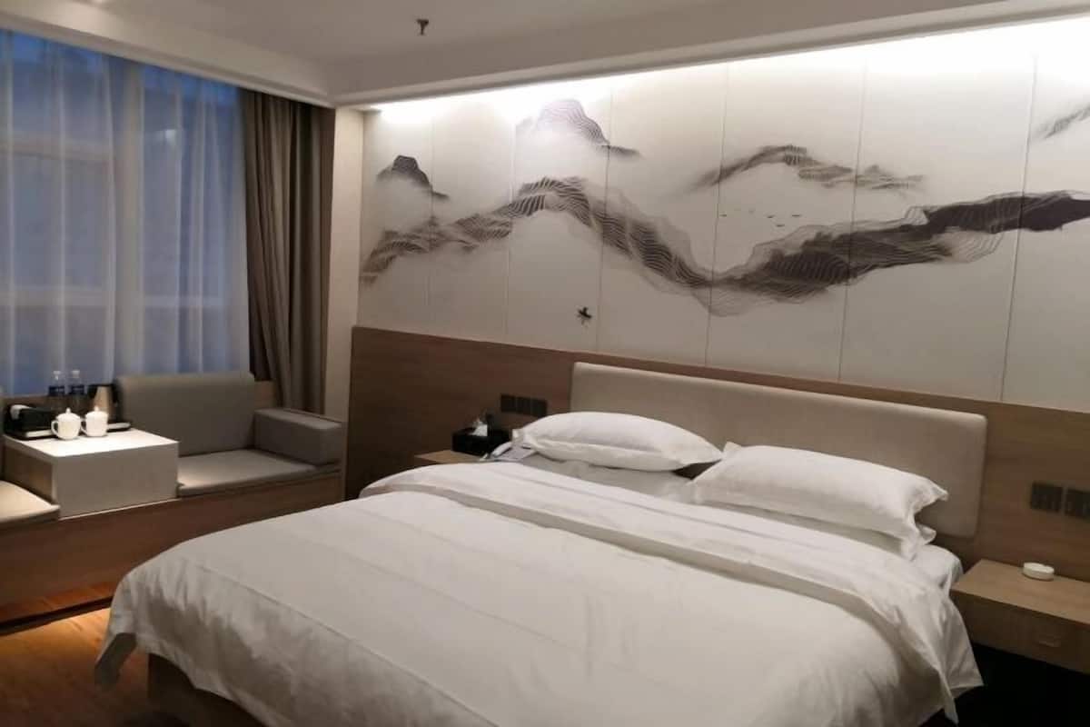 A hotel room with a bed, a seating area, a wall with artwork, and a window with curtains.