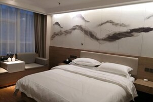 Una habitación de hotel con cama, zona de estar, una pared decorada con obras de arte y una ventana con cortinas.